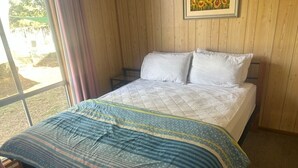 Un dormitorio con cama, ventana con cortinas y un cuadro en la pared.
