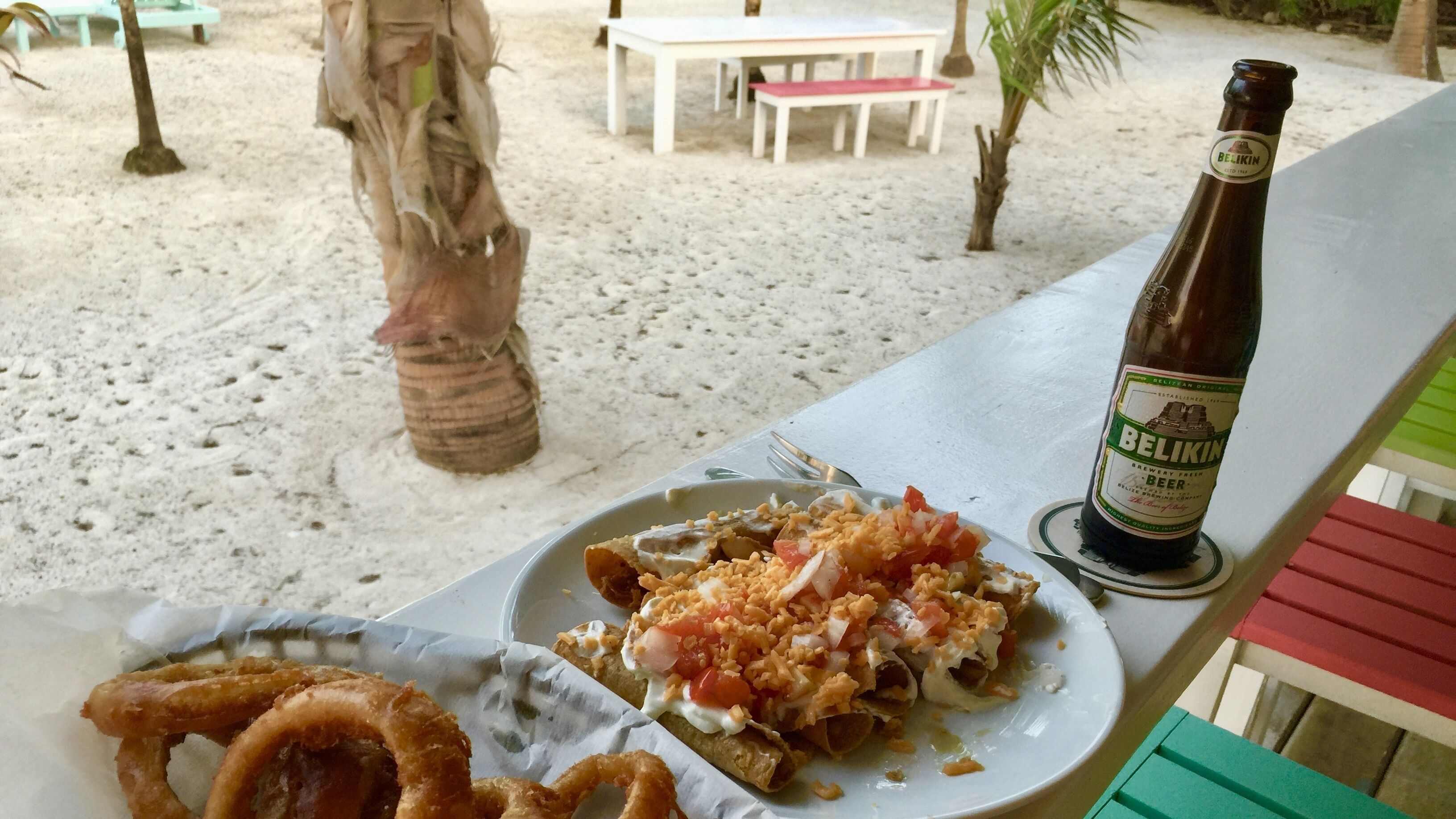 Un plato de nachos y aros de cebolla sobre una mesa con una botella de cerveza Belikin.