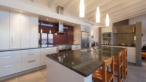 Une cuisine moderne dotée d’un îlot central, d’appareils électroménagers en acier inoxydable et de luminaires suspendus.