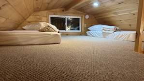 Une chambre mansardée chaleureuse, avec deux lits, une grande fenêtre et un plafond en bois.