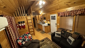 Un intérieur de chalet chaleureux, avec un revêtement en bois, une cheminée, un canapé, un coin repas et une cuisine.