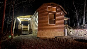 Une cabane en bois dotée d’un porche et d’une petite terrasse, entourée d’arbres.