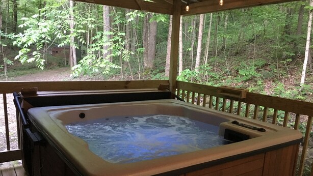 Un bain à remous installé sur une terrasse en bois, avec vue sur une forêt.