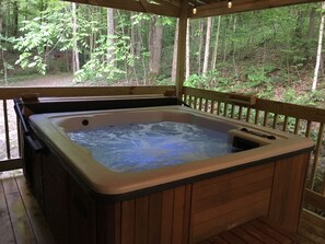 Un bain à remous installé sur une terrasse en bois, avec vue sur une forêt.