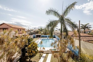 A swimming pool surrounded by palm trees and a building with a tiled roof.