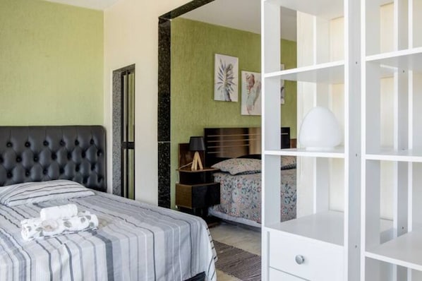 A hotel room with a bed, a nightstand, a lamp, and a white shelving unit.