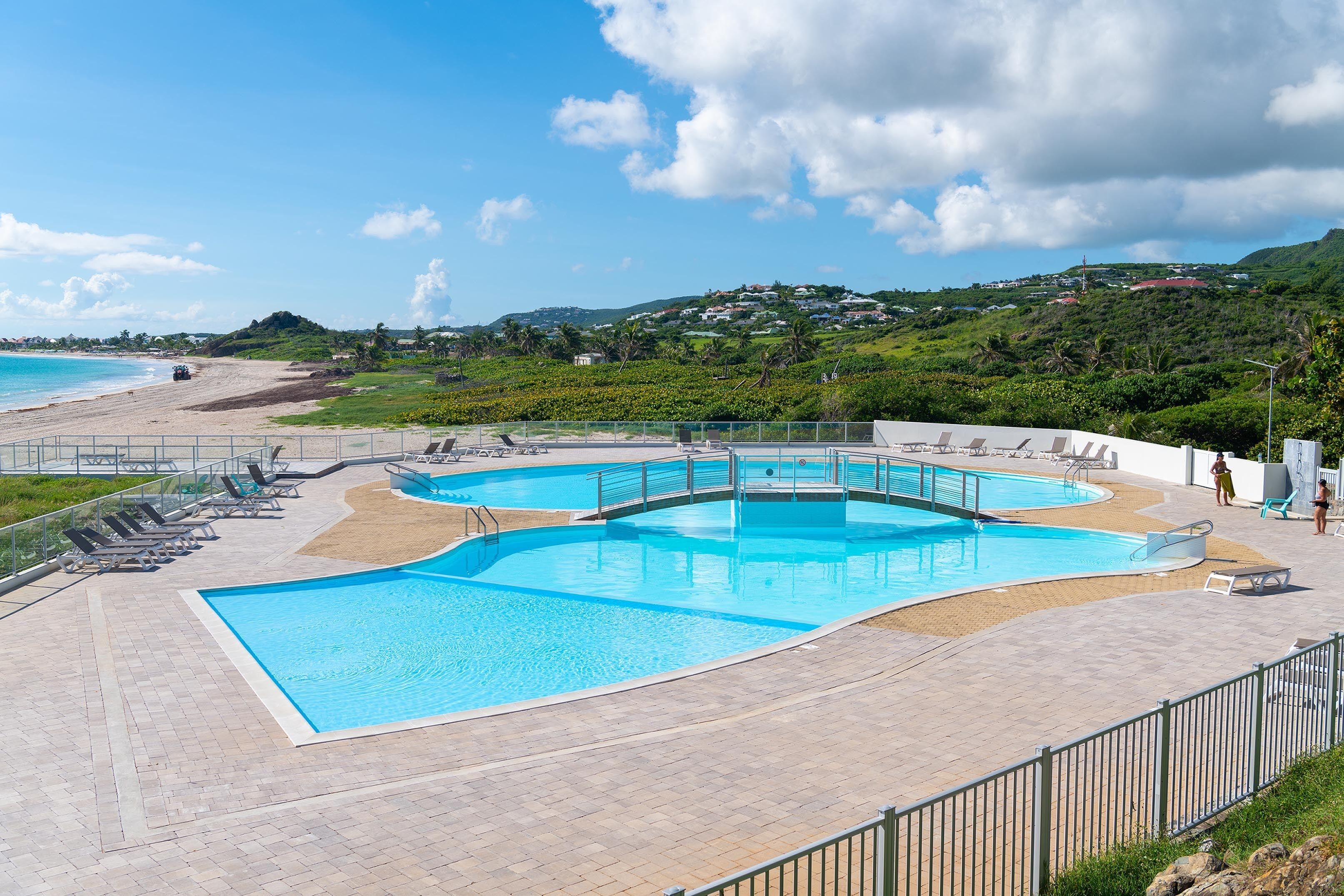 A swimming pool with a curved design, surrounded by lounge chairs and a paved deck.