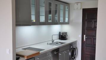 A compact kitchen with grey cabinets, a coffee machine, a washing machine, and a small countertop.