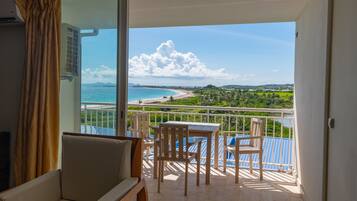 A balcony with a table and chairs, overlooking a beach and green landscape.