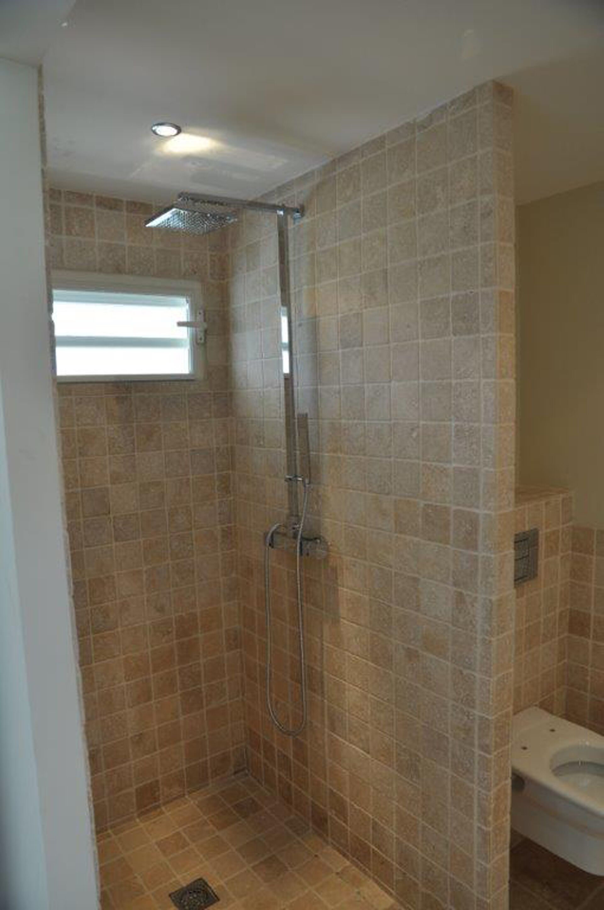 A small, tiled shower room with a window and a toilet.