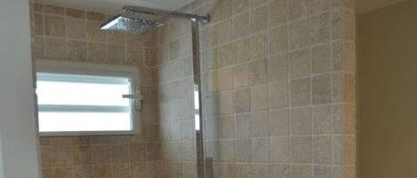 A small, tiled shower room with a window and a toilet.