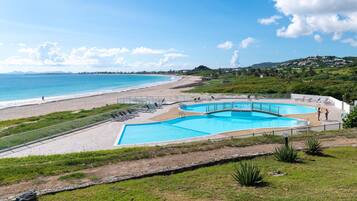 A beachside resort with a swimming pool, beach access, and a view of the ocean.