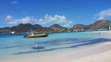 A beach with clear turquoise water, a yellow boat, and distant mountains.
