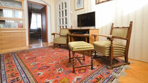 A room with a large red patterned rug, wooden furniture, a television, and framed artwork on the wall.