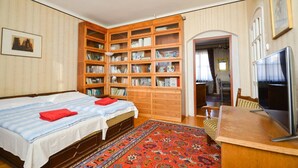 A hotel room with two beds, a large bookshelf, a TV, and a patterned rug.