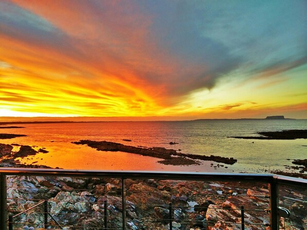 A sunset over a rocky coastline with a metal railing in the foreground. - Stanley View Beach House (Cowrie Point)
