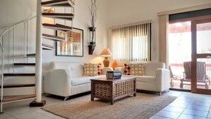 Ein Wohnzimmer mit einem weißen Sofa, einem Couchtisch, einer Treppe und einem großen Fenster mit Jalousien.
