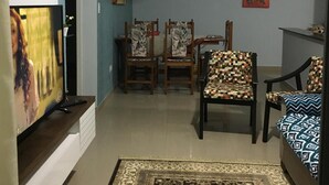 Un salon équipé d’un téléviseur à écran plat, d’un ventilateur de plafond, d’un coin repas avec des chaises et une table, et d’un tapis à motifs.