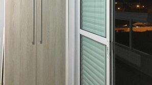 Une pièce dotée d’une porte-fenêtre coulissante, d’une armoire en bois avec deux poignées et d’une fenêtre avec des stores.