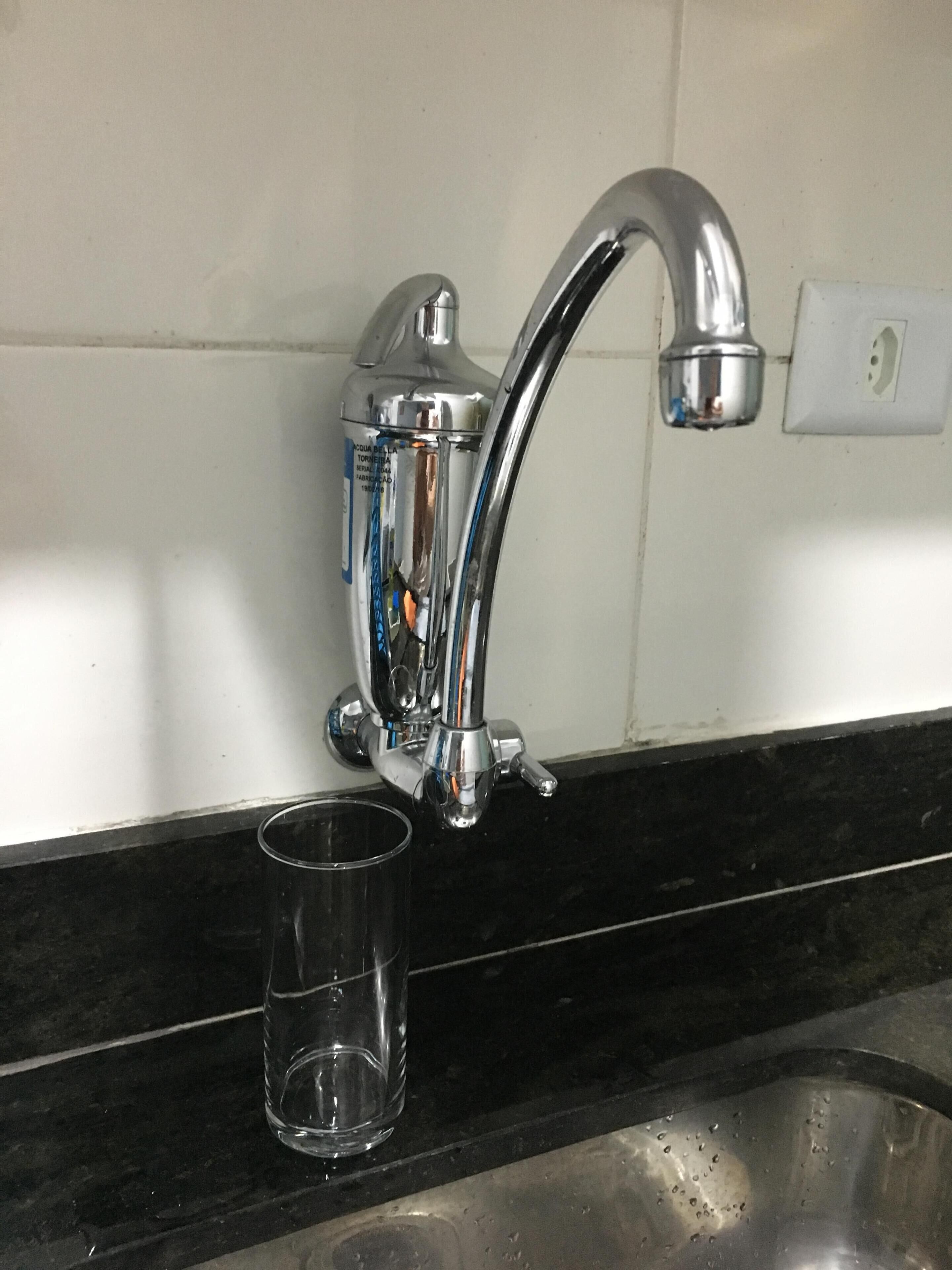 Ein Küchenspüle mit einem chromfarbenen Wasserhahn, einem Glas und einer weiß gefliesten Wand.