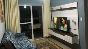 Un salon avec un téléviseur fixé sur un meuble mural, un canapé, un ventilateur de plafond et une porte-fenêtre coulissante donnant sur un balcon.