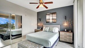 Une chambre moderne avec un grand lit, un ventilateur de plafond, des lampes de chevet et une vue sur l’extérieur grâce à une porte-fenêtre coulissante.