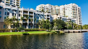 Un hôtel à plusieurs étages doté de balcons, avec un plan d’eau au premier plan et un ciel bleu dégagé.