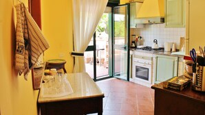 A kitchen with a dining table, a stove, and a window with curtains. - Between Catania and Syracuse,countryside Villa  with private pool 1km from beach (Brucoli)