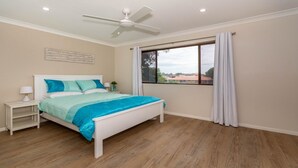 Ein Schlafzimmer mit Bett, Nachttisch, Deckenventilator und einem Fenster mit Vorhängen.