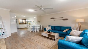 Ein modernes Wohnzimmer mit einem blauen Sofa, einem Couchtisch und einem Essbereich mit weißen Stühlen.