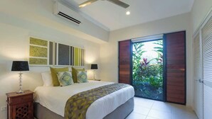 Un dormitorio con una cama grande, un ventilador de techo y un ventanal corredera a un jardín.