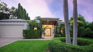 Una casa moderna con garaje, césped bien cuidado y plantas tropicales.