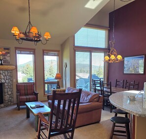 A spacious living area with a stone fireplace, a brown sofa, a dining table with chairs, and a kitchen island.