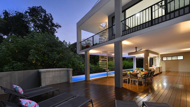 Una casa moderna con terraza de madera, piscina exterior y zona de comedor con mesa y sillas.