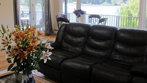 A living room with a black leather sofa, a vase of flowers, and a view of a lake through large windows. - Lake front - Upper floor - no animal- allergies  (Federal Way)