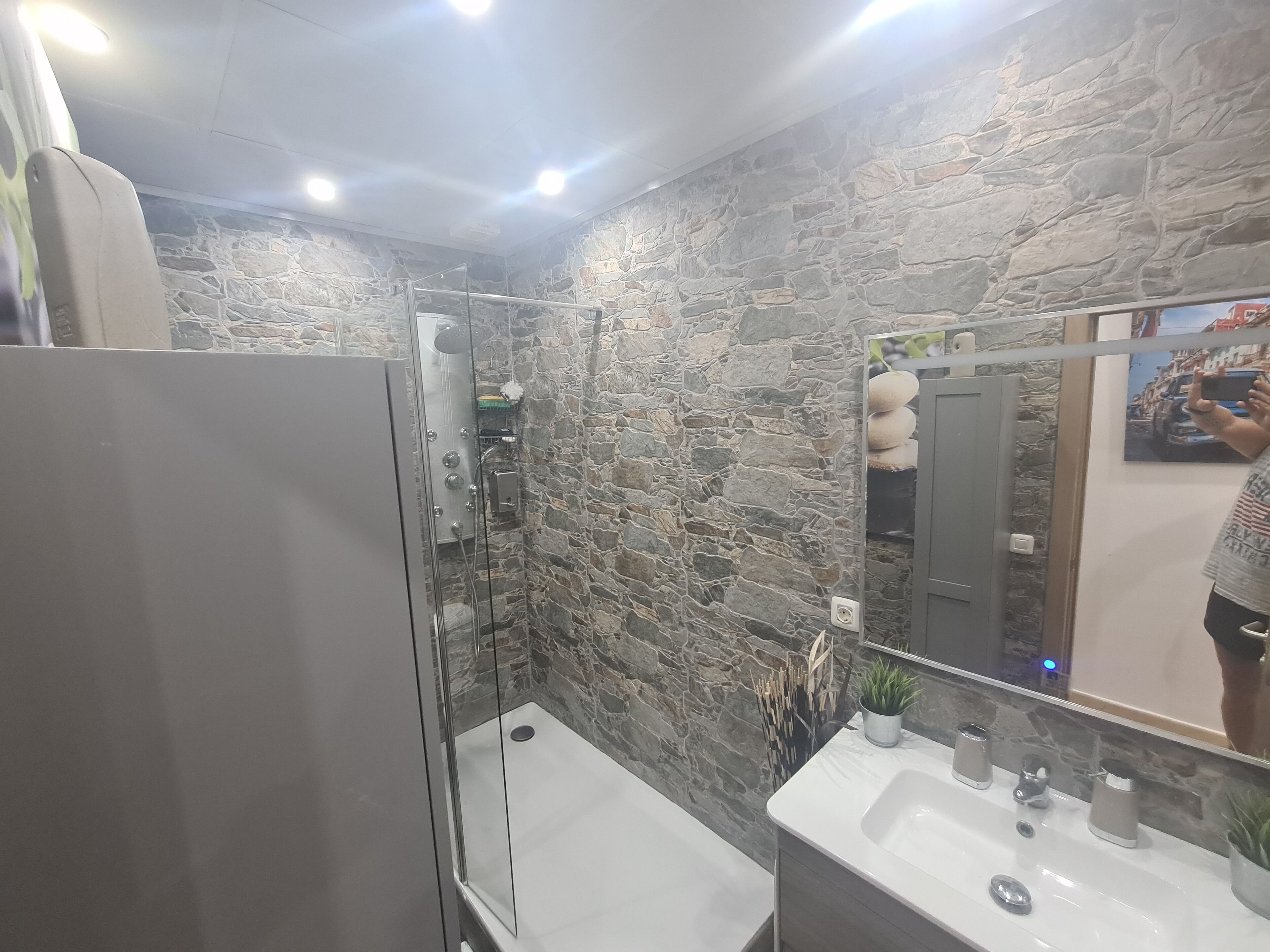 A bathroom with a stone wall, a glass shower enclosure, and a sink with a mirror.