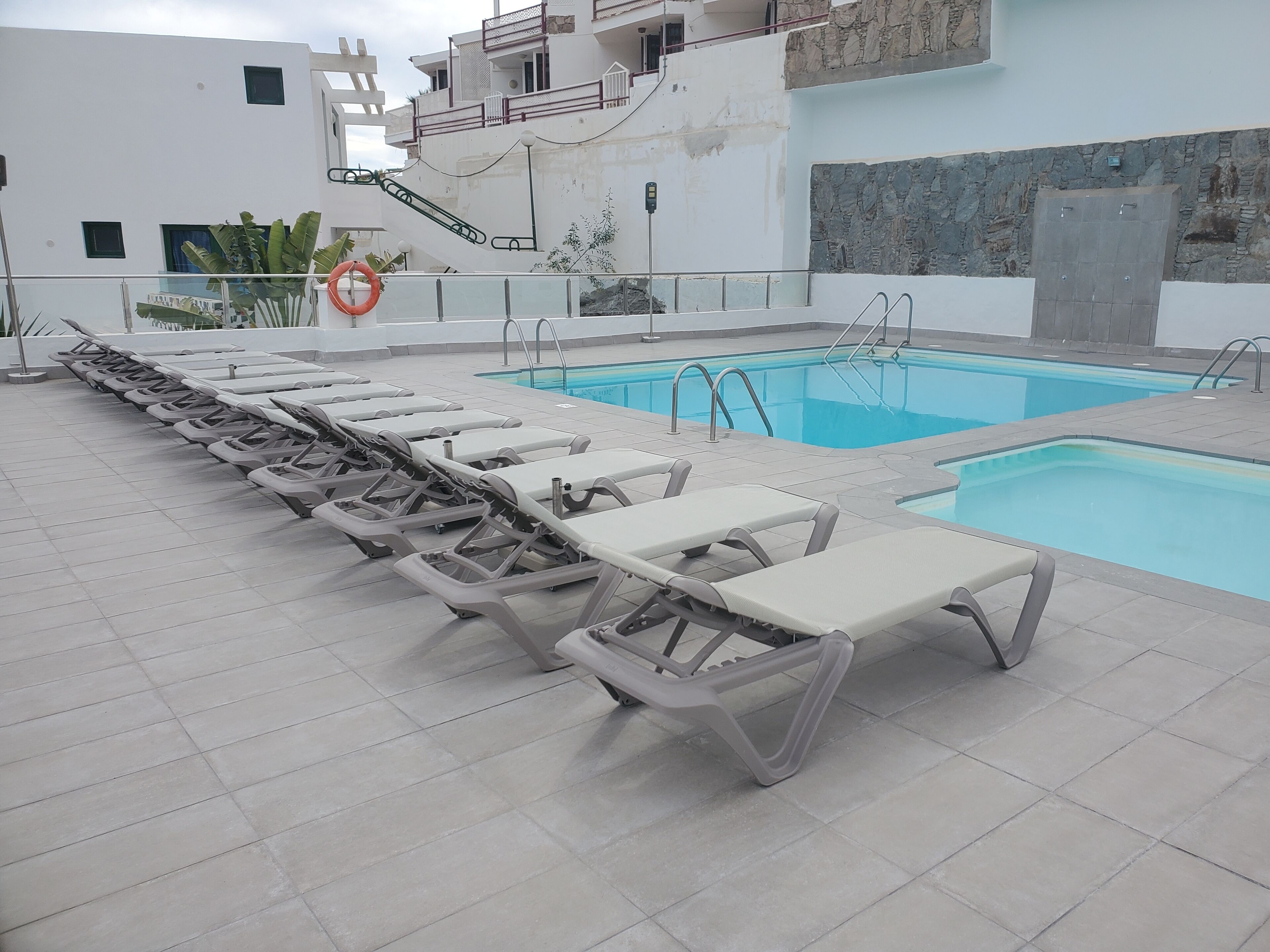 A swimming pool area with multiple sun loungers and a lifebuoy.