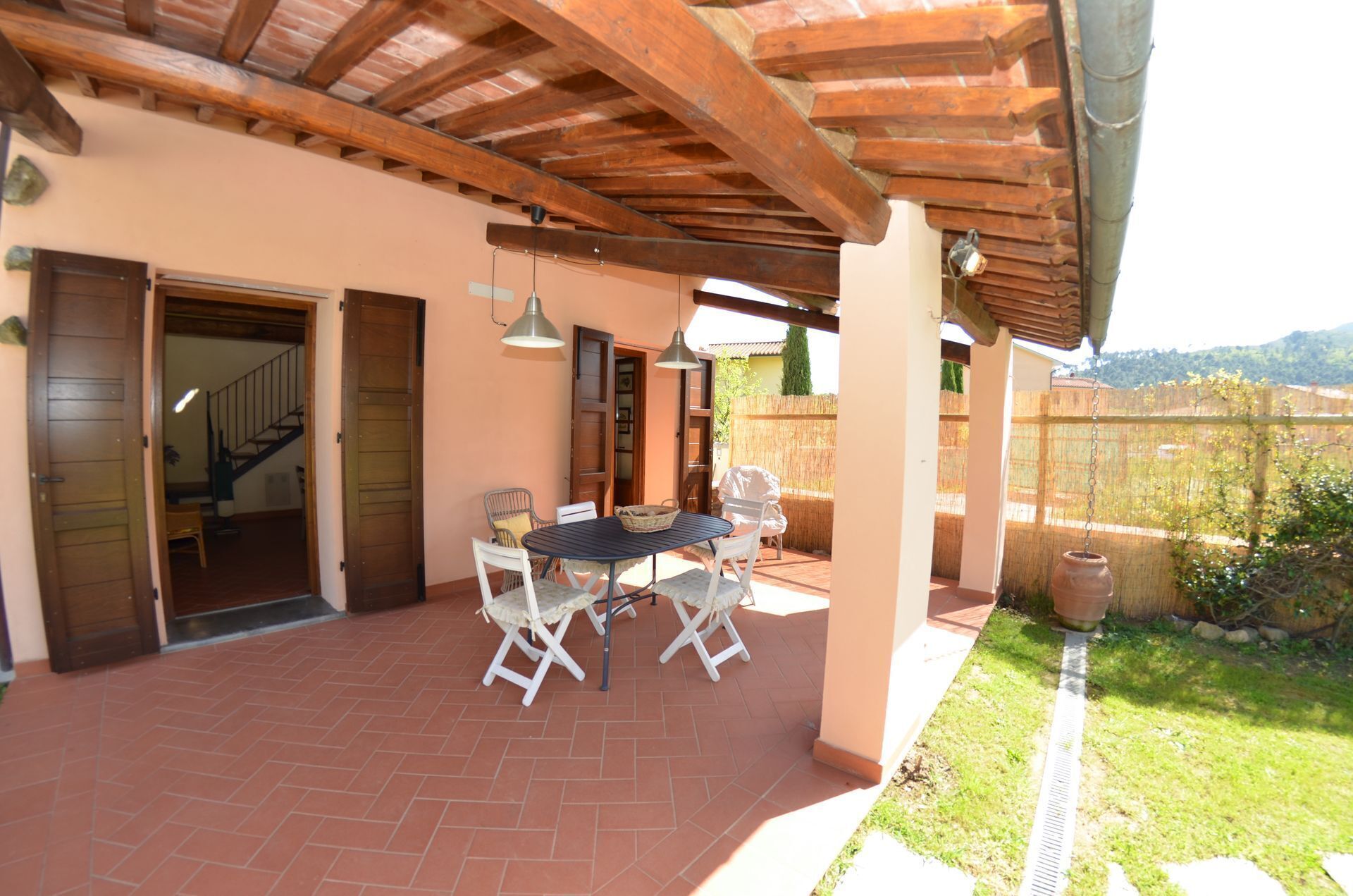 Un patio techado con una mesa y sillas, un lámpara colgante, y vistas a un paisaje montañoso.