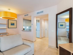 A modern hotel room with a sofa, a dining area, a kitchen, and a bathroom.