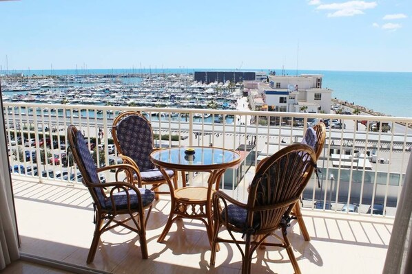 A balcony with wicker chairs and a glass table overlooking a marina with numerous boats.