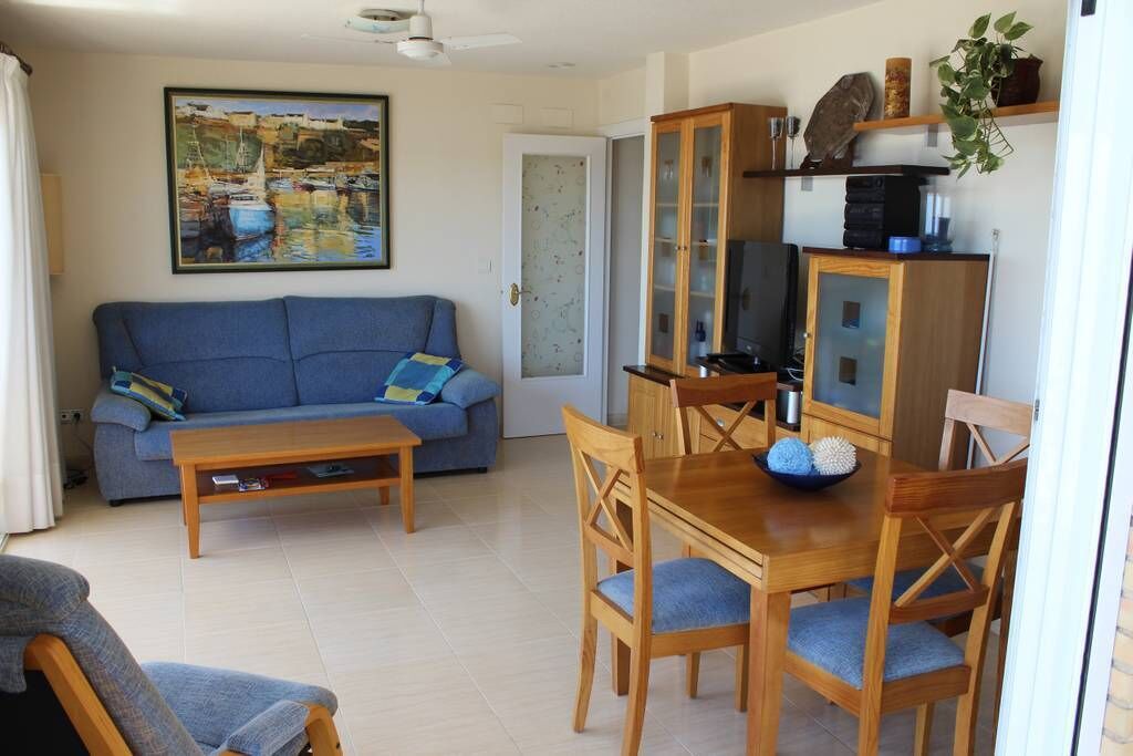 Un salon avec un canapé bleu, une table à manger en bois et des chaises. Il y a un tableau au mur et un meuble sur lequel se trouve un téléviseur.