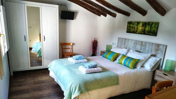 A bedroom with a bed, wooden beams, a TV, a painting, and a wooden chair. - Rural house with garden and barbecue in the Moncayo area. (Bulbuente)
