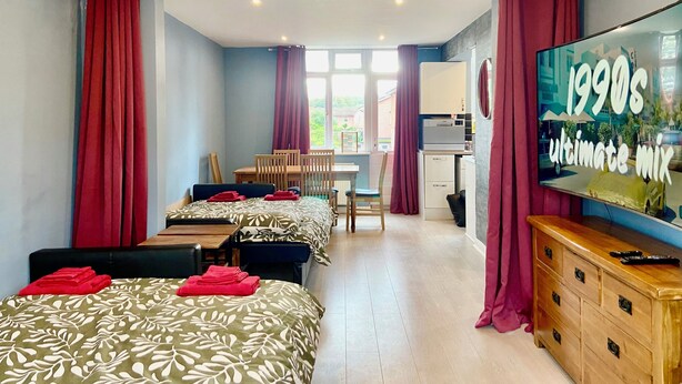 Habitación de hotel con dos camas, una mesa de comedor, sillas, un televisor y una kitchenette.