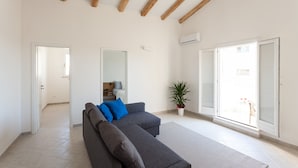 Un salón amplio con un sofá seccional gris, una planta en maceta y un gran ventanal corredero que da a un espacio exterior.