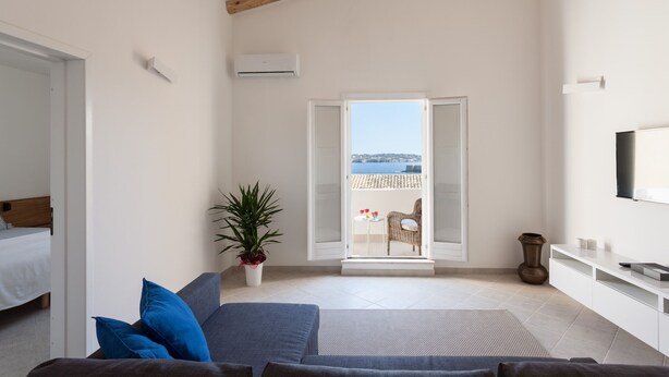 A modern room with a bed, a sofa, a potted plant, and a balcony with a view. - Attico Mansion, Ortigia (Siracusa)
