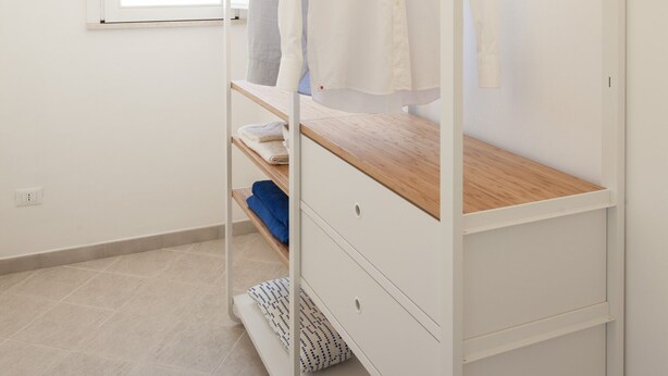 Una cama individual con cabecera de madera, un armario blanco y una ventana con cortinas.