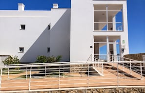A modern building with a white facade, a staircase leading to a balcony, and a clear blue sky. - Penthouse Apartment With Communal Pool & Spectacular Lagoon Views. (Fuseta)