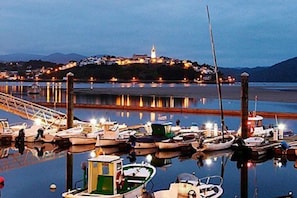 A marina with boats docked, a lighthouse in the background, and a bridge leading to the shore.