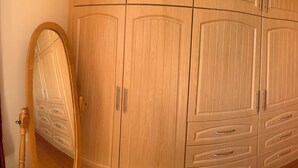 Ein Holzkleiderschrank mit mehreren Schubladen und Türen, ein Spiegel und eine Holztür in einem Raum mit Holzboden.