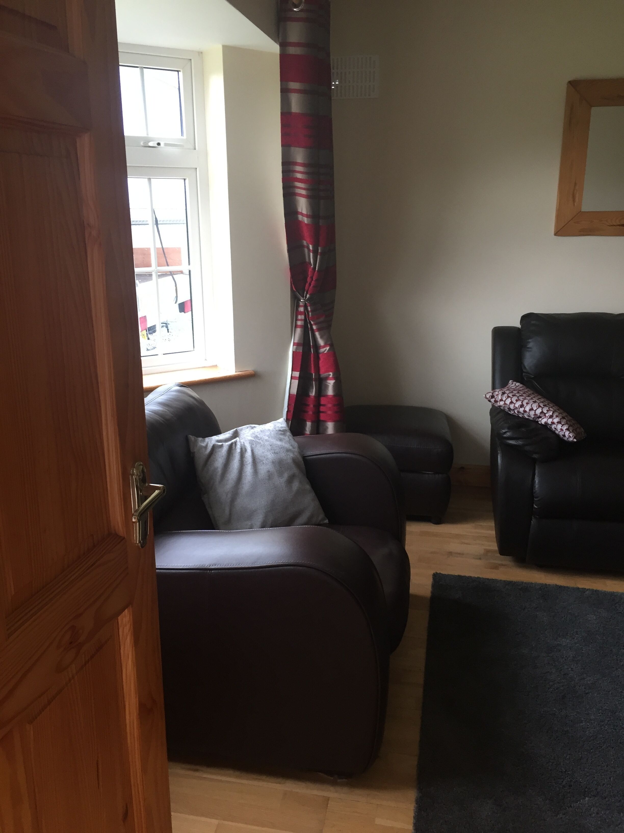 A living room with a dark brown sofa, a black leather armchair, and a patterned curtain.